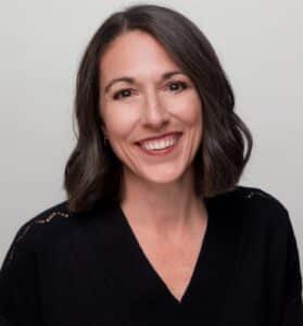 Portrait of a woman smiling in a black sweater against a gray background.